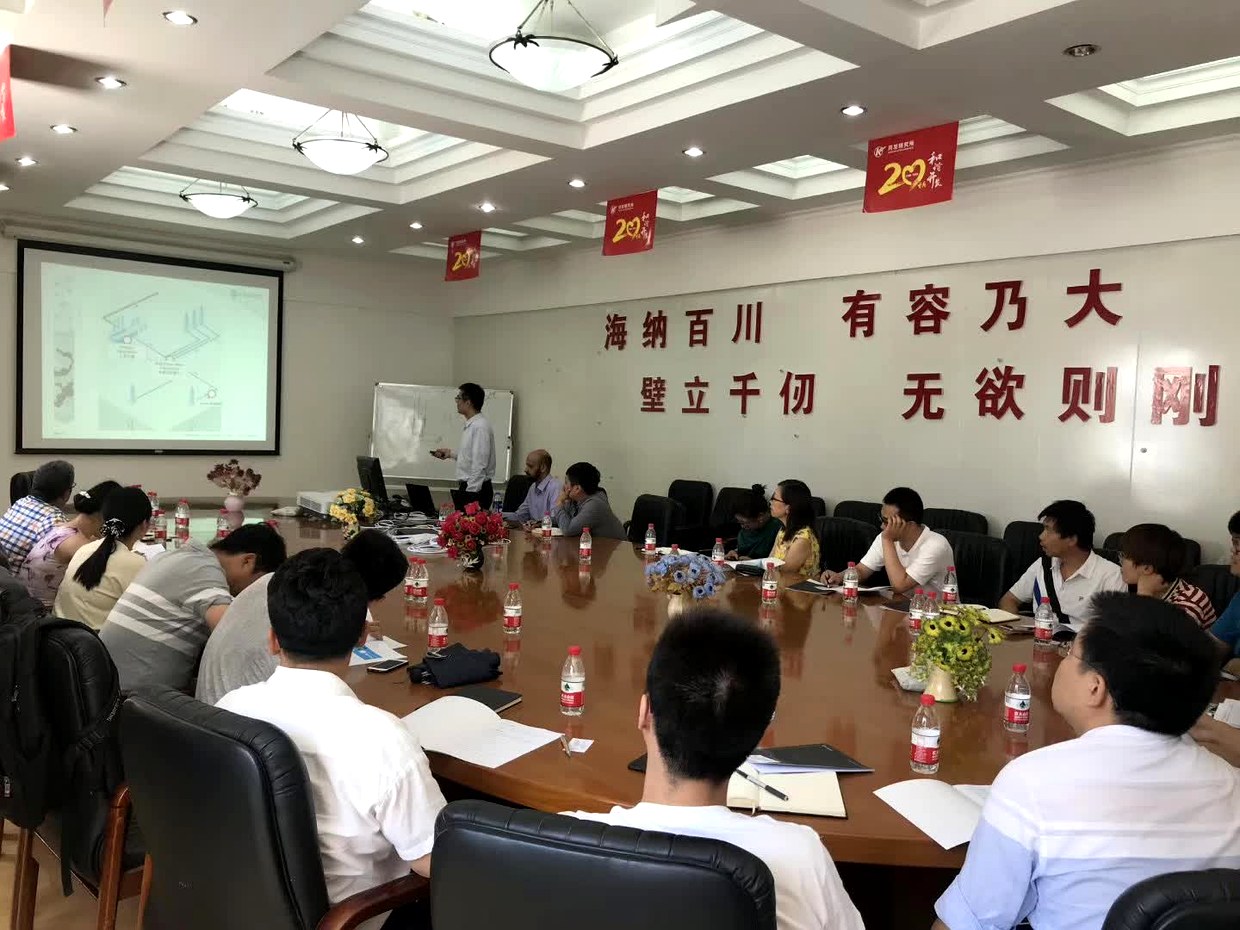 新疆油田站交流现场全景，U 形会议桌两侧坐满参会人员，主讲人在白板前讲解