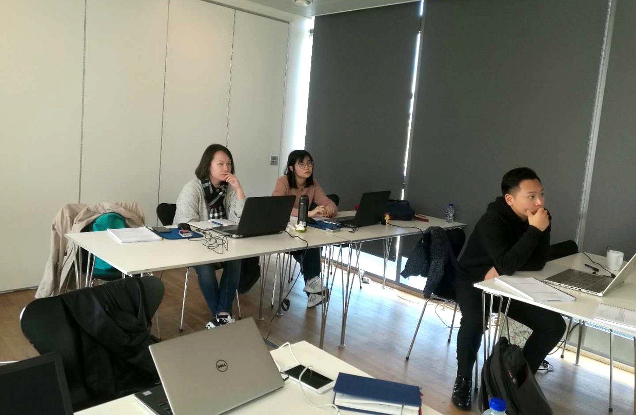 三位学员并坐在桌前各自操作笔记本电脑，教室后方遮光帘半开