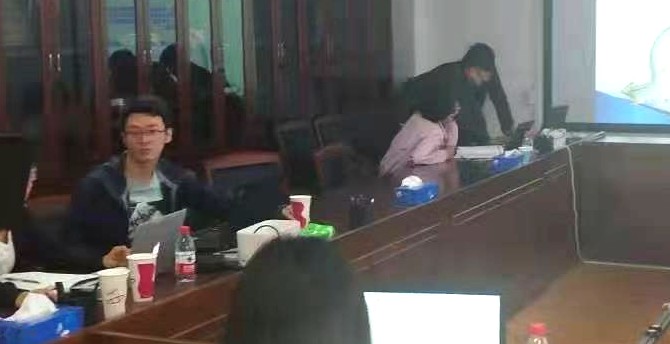 会议室内的交流现场，与会人员一边查看投影内容一边对照桌面资料做记录