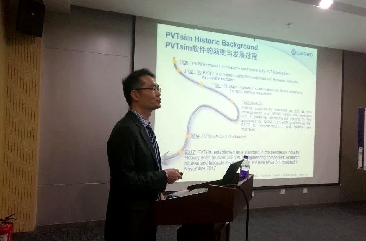 投影屏幕显示 PVTsim Historic Background 时间轴页面，讲解人员手持翻页器站在讲台旁