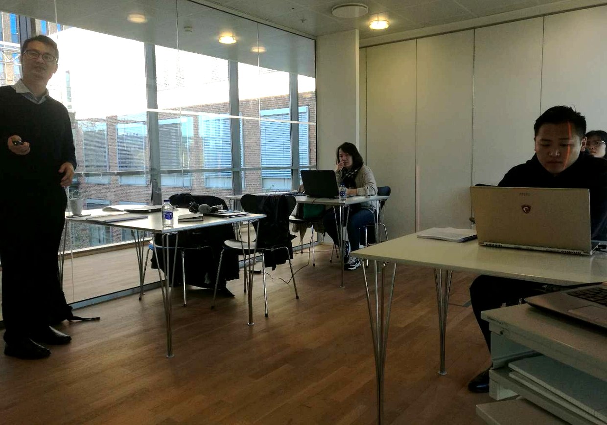 我方人员与学员在教室内，左侧一位公司人员站立，右侧两位学员正对着笔记本电脑屏幕
